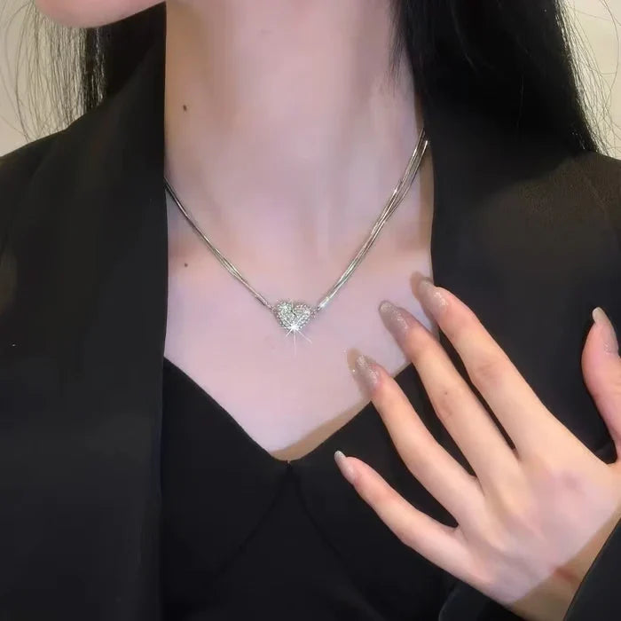 Magnetic Love Patchwork Necklace - A hand with glittery nude nails rests near the neck, showing the same silver heart pendant necklace, black outerwear over v-neck top
