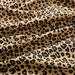 Hooded Jacket - Close-up of folded leopard print fabric with a beige base, black spots and tan spot centers, showing soft horizontal wrinkles