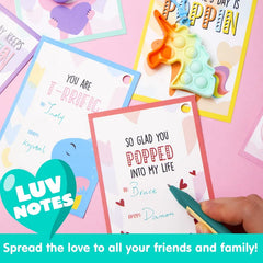 Handwritten notes on decorative cards next to a unicorn pop fidget, showing valentines day cards with pop fidget keychains being personalized.