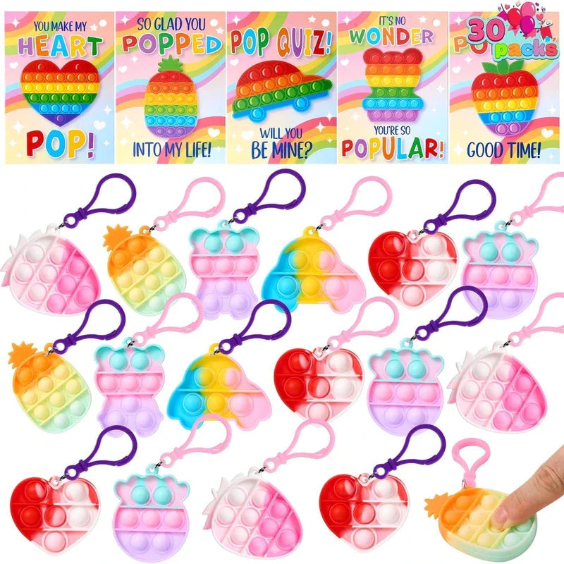 Assorted pop fidget keychains (pineapple, bear, heart, car shapes) and matching greeting cards; valentines day cards with pop fidget keychains are shown.