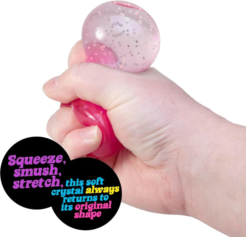 A hand squeezing a pink glittery schylling needoh groovy jewel squeeze toy, with text describing it can be squeezed and returns to original shape.
