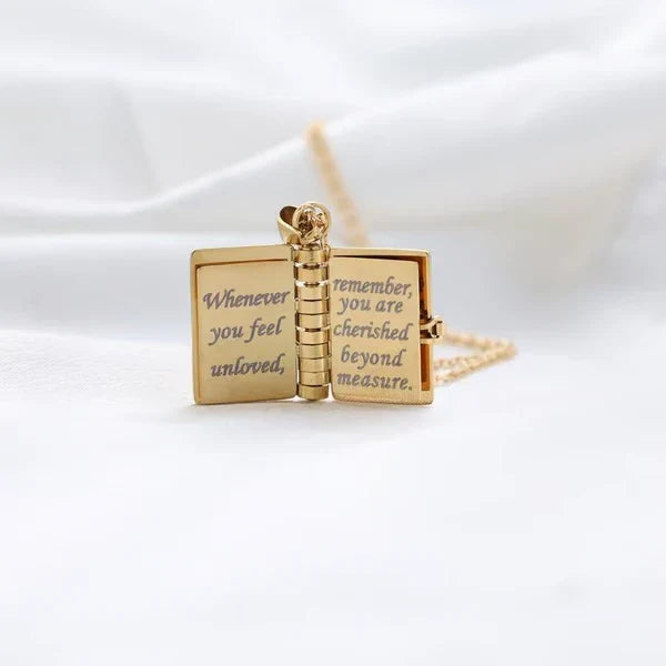 Book Necklace - Open gold book pendant standing upright, showing inside engraved text across its two inner pages, chain visible behind