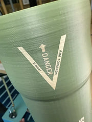 Close-up of green curved item surface with a white V-shaped danger marking and upward arrow.