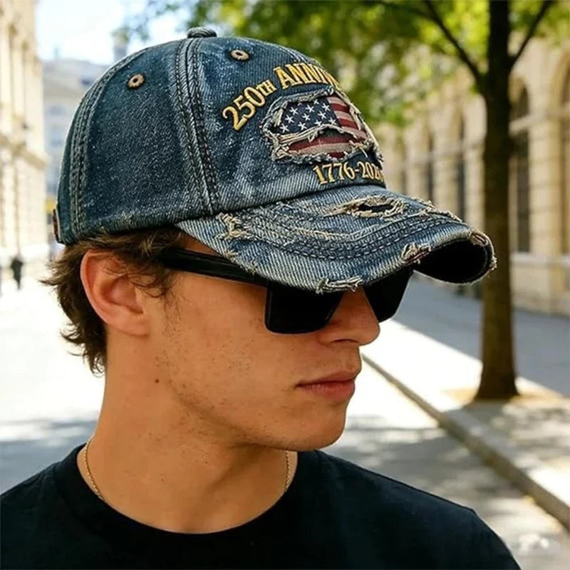 Gorra de béisbol conmemorativa: vista de perfil de un hombre joven al aire libre, usando una gorra de béisbol de mezclilla desgastada y gafas de sol negras, sobre una acera pavimentada