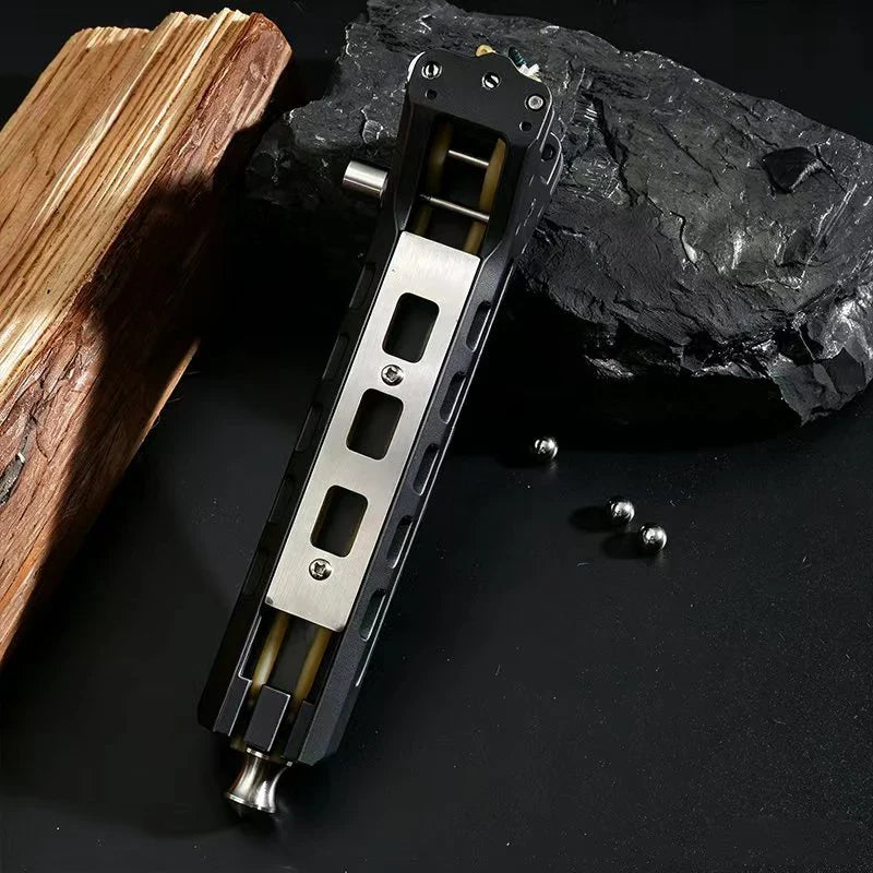 Angled top view of a black and silver shooting toy resting on dark rock with steel balls and a wooden block
