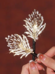 Pfauenfeder Haarschmuck - Nahaufnahme eines goldfarbenen Kristall-Pfauenfeder-Haarschmucks mit Perlen, gehalten von einer Hand mit Verlauf-Nagelkunst