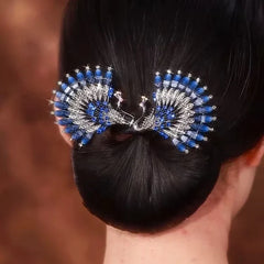 Pfauenfeder Haarschmuck - Rückansicht eines tiefen Dutt einer Frau, verziert mit einem blau-silbernen Pfauenfeder-Haarschmuck mit glitzernden Verzierungen.