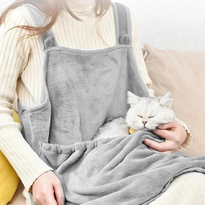 Delantal portabebés para gato con bolsillo acogedor - Persona con suéter color crema usando un delantal gris de felpa con un gato blanco durmiendo en el bolsillo