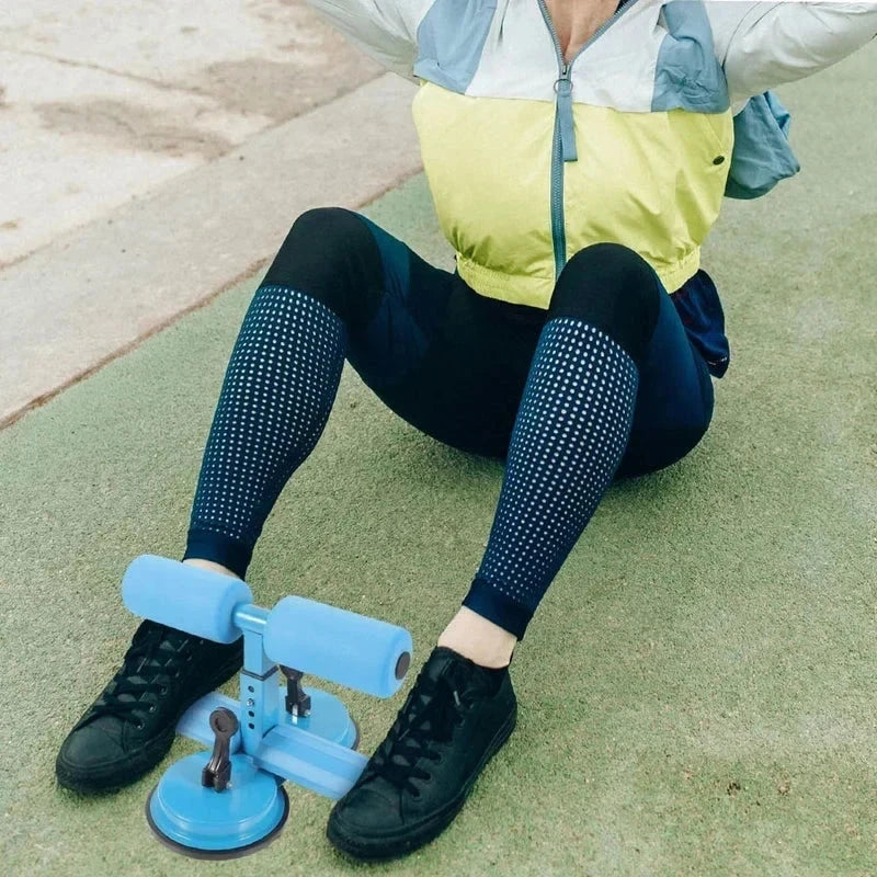 Sit Up Assistant Device - Person seated on green textured ground, feet positioned under the sit-up assistant’s foam rollers.