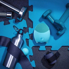 Light blue facial cleansing brush placed among workout equipment on interlocking foam mats
