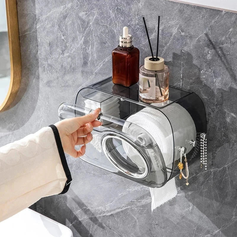 Cotton Pad Dispenser Holder - Smoky gray wall mount tissue box with a hand lifting the upper lid, items placed on top, with hanging decorations on the side.
