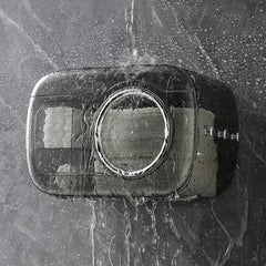 Cotton Pad Dispenser Holder - Closed transparent gray wall-mounted dispenser with water streaming over it, droplets visible, mounted on a wet gray tiled surface with white rolls inside.