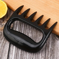 Pulled Pork Shredder Claws - Single black meat shredding tool resting on the edge of a wooden cutting board next to a lemon slice on a wood-grain surface