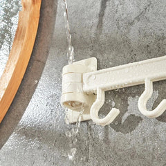 Adhesive Wall Hooks - Close-up of the hinged joint of a white hook rack, with running water flowing over it on a wet tiled surface.