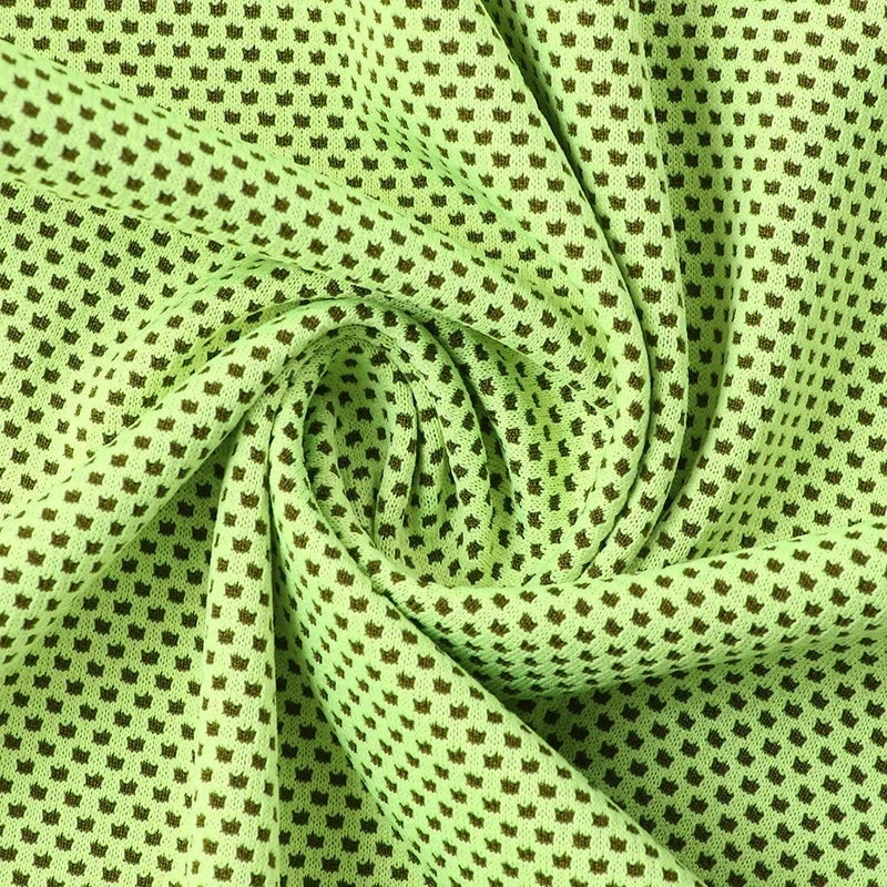 Close-up of twisted light green cooling towel fabric with a dark repeating dot pattern.