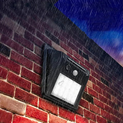 A lit motion sensor light mounted on a red brick wall during heavy rainfall at night