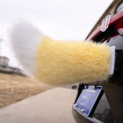 A car moving tail with yellow and white faux fur mounts on the back of a dark car with a visible license plate.