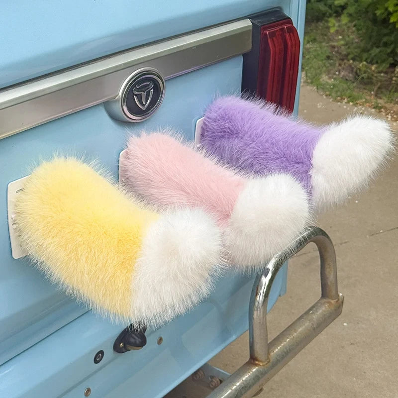 Three colorful faux fur car moving tails attach to the rear of a light blue vehicle.