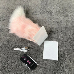 A pink and white plush car moving tail, a USB charging cable, a remote control, and an adhesive pad lie on a gray carpet.