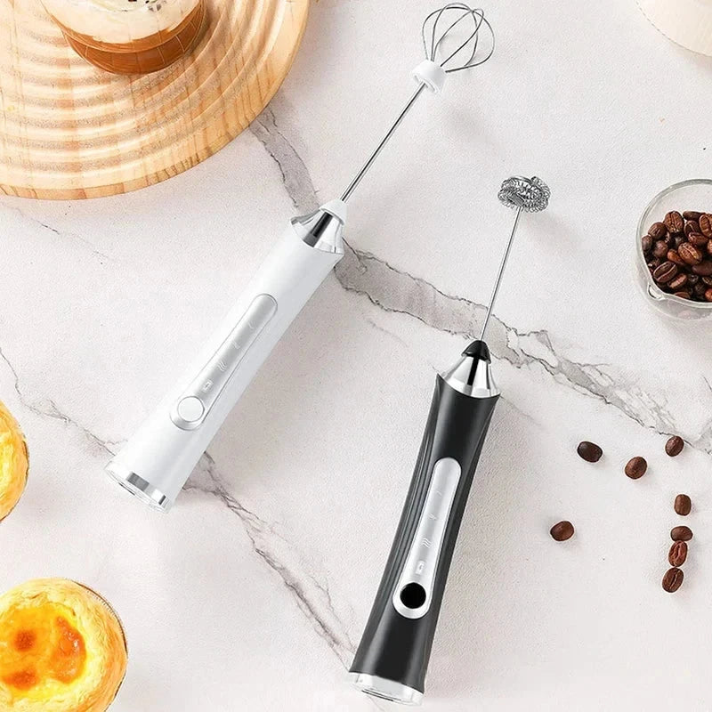 Batidor eléctrico: dos batidoras eléctricas manuales (blanca y negra) con diferentes accesorios batidores descansan sobre una superficie de mármol junto a granos de café y pasteles