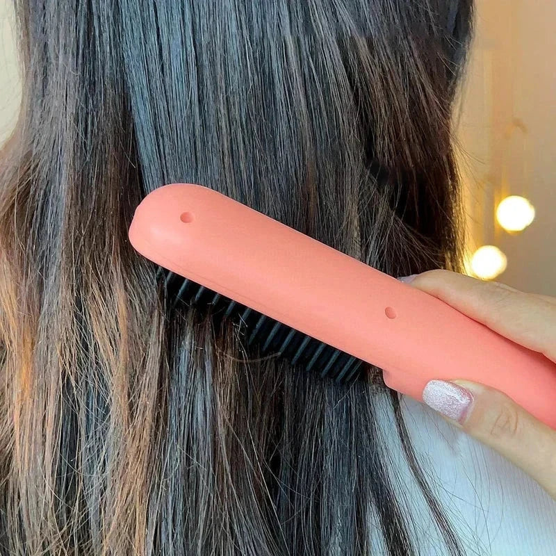 Coral pink hair straightener brush being run through long dark hair, held by a hand