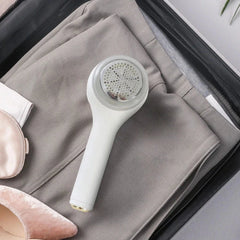 Afeitadora de tela blanca colocada sobre pantalones grises doblados dentro de equipaje de viaje