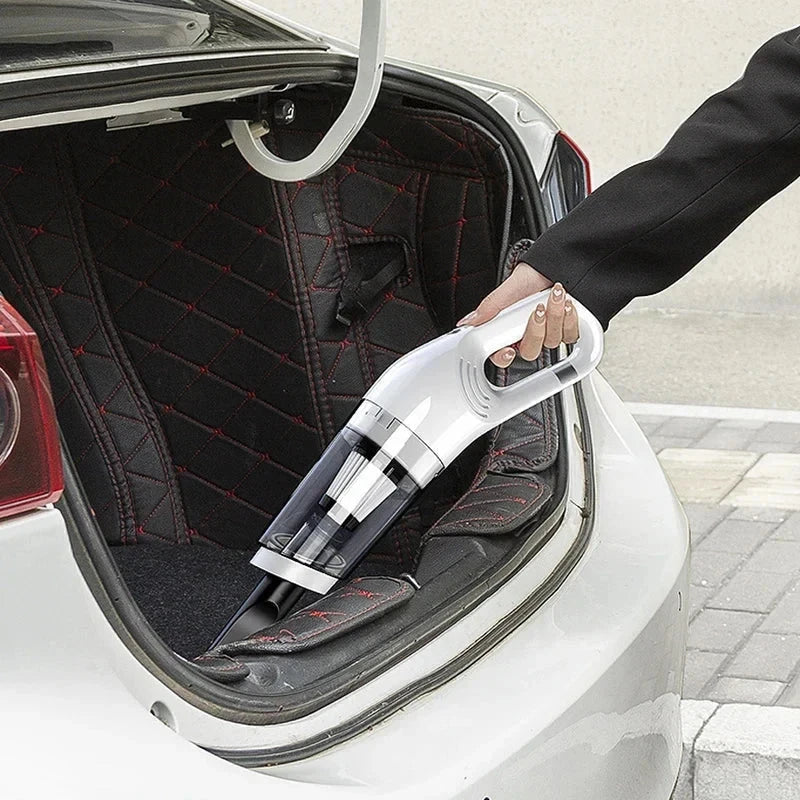 A hand holds a handheld vacuum to clean the quilted fabric lining of a car trunk