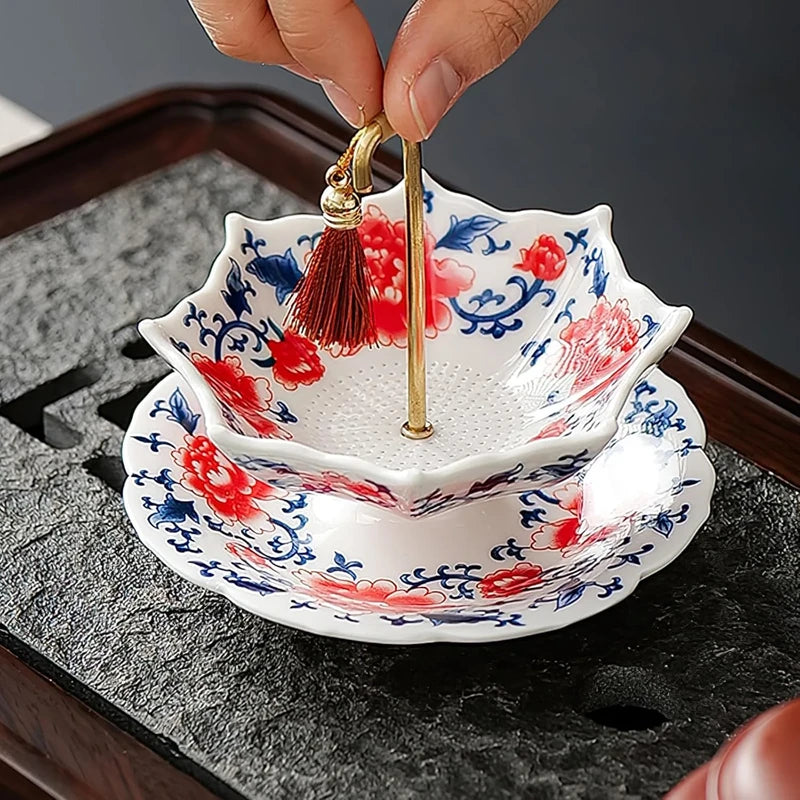 Fingers holding red blue floral ceramic tea filter with red tassel gold rod on dark tray