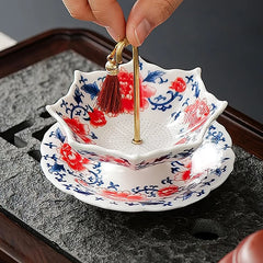 Fingers holding red blue floral ceramic tea filter with red tassel gold rod on dark tray