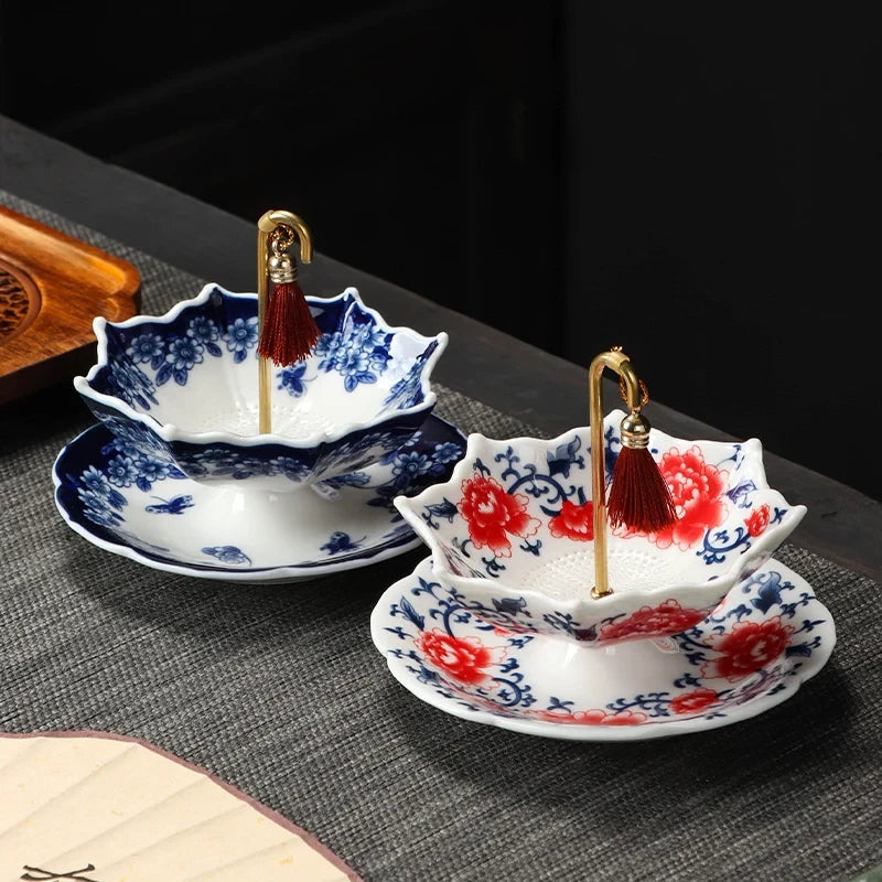 Ceramic Tea Filter - Two ceramic tea filters, one blue white floral one red blue floral, with tasseled gold rods on grey mat