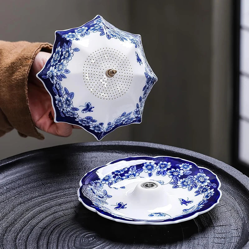 Hand holding a blue floral umbrella-shaped ceramic tea filter above its matching ceramic base dish