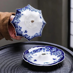 Hand holding a blue floral umbrella-shaped ceramic tea filter above its matching ceramic base dish