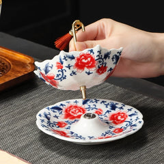 Hand holds decorative floral ceramic tea filter above its matching patterned base on a textured mat