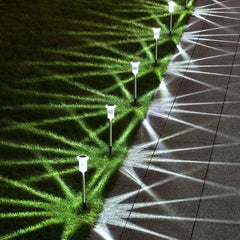 Row of lit solar garden lights along paved walkway edge, casting geometric light patterns on path and grass