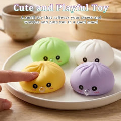 Sensory Bubble - Four pastel colored steamed bun shaped squish toys sit on a light plate; a finger presses the yellow toy, with a teacup and steamer in the background.