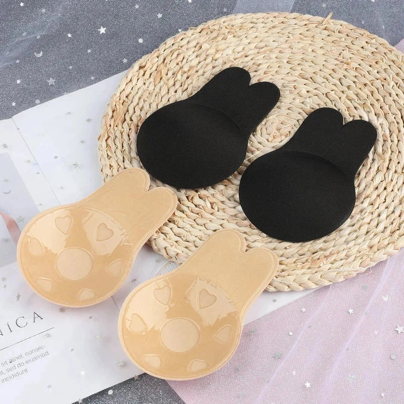 Nipple Concealers - Two pairs of rabbit-ear shaped nipple covers laid on a woven mat, showing black fabric sides and beige adhesive sides
