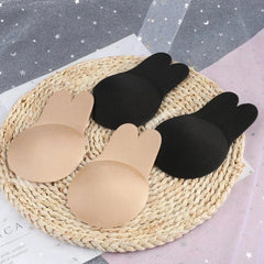 Nipple Concealers - Two pairs of rabbit-ear shaped nipple covers laid on a woven mat, showing black and beige fabric outer sides