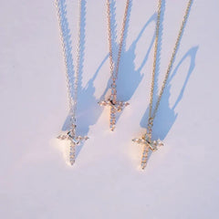 Faith Necklace - Three cross necklaces in silver, rose gold, and gold tone laid flat in a row on a light surface, casting shadows