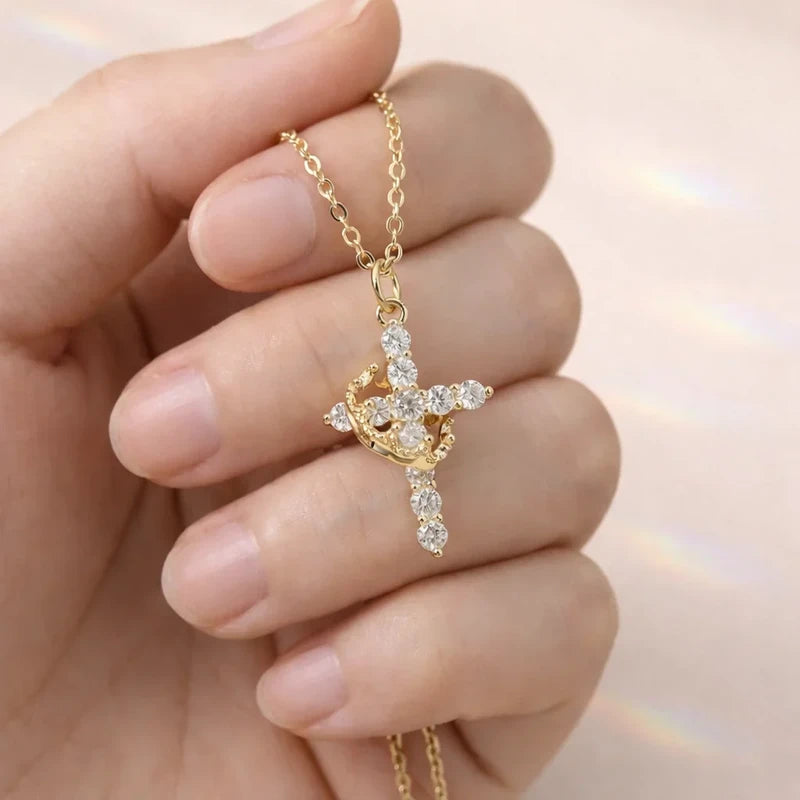 Faith Necklace - Close-up of a hand holding a gold crystal-studded cross pendant attached to a thin gold chain.