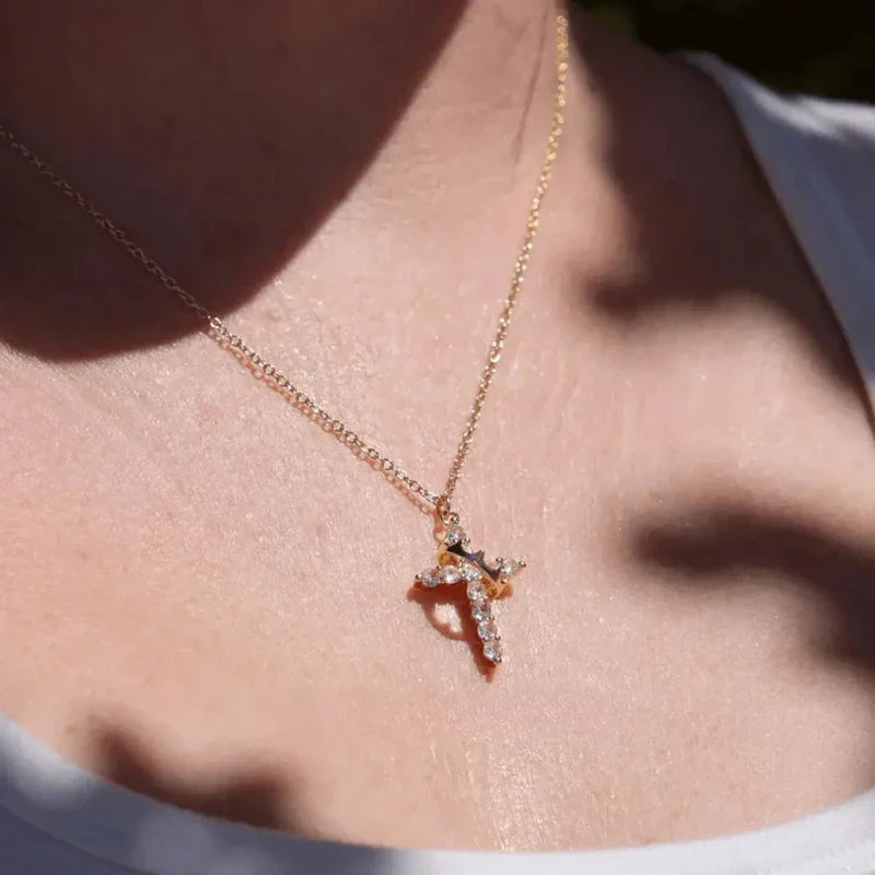 Faith Necklace - Close-up of a gold crystal-adorned cross necklace worn on a person’s upper chest and neck.