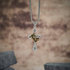 Crown Pendant - Silver cross pendant necklace with gold crown detail, displayed against a blurred light brown background with dark stone props at bottom corners