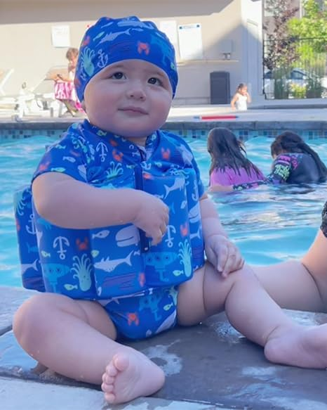 Toddler in blue marine print kids buoyancy swimsuit sits at pool edge