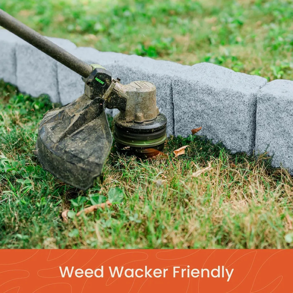 Weed wacker trimming grass next to installed grey stone landscape edging