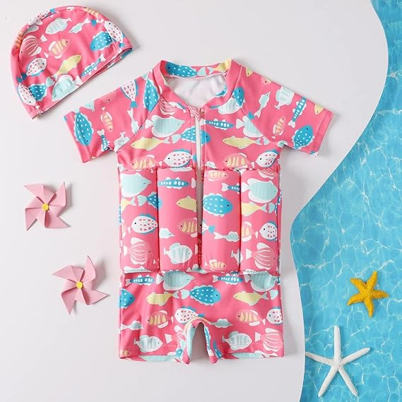 Pink fish print kids float swimsuit with matching swim cap, flat lay with beach decor