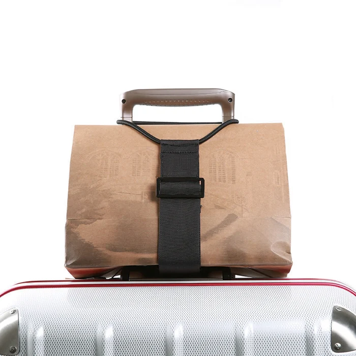 Luggage strap securing a paper bag on top of a rolling suitcase